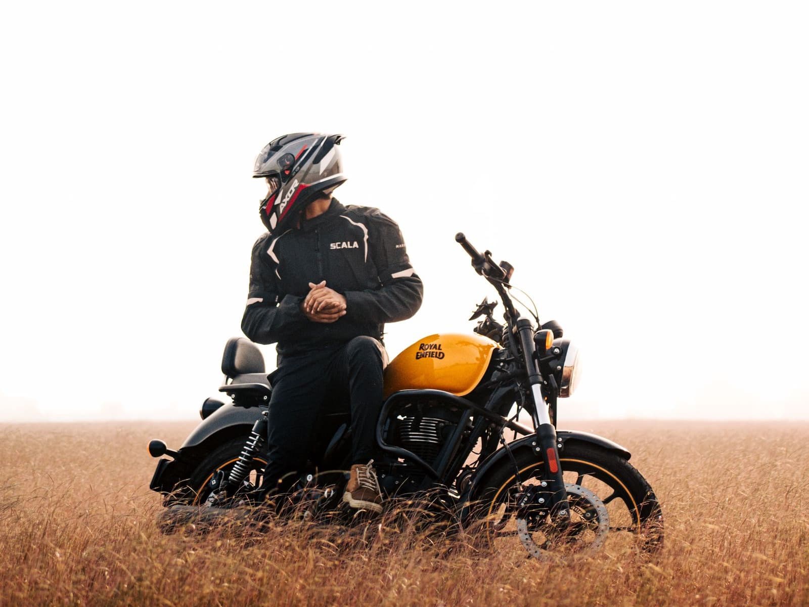 A rider on a yellow Royal Enfield Meteor 350 in a field of dry grass
