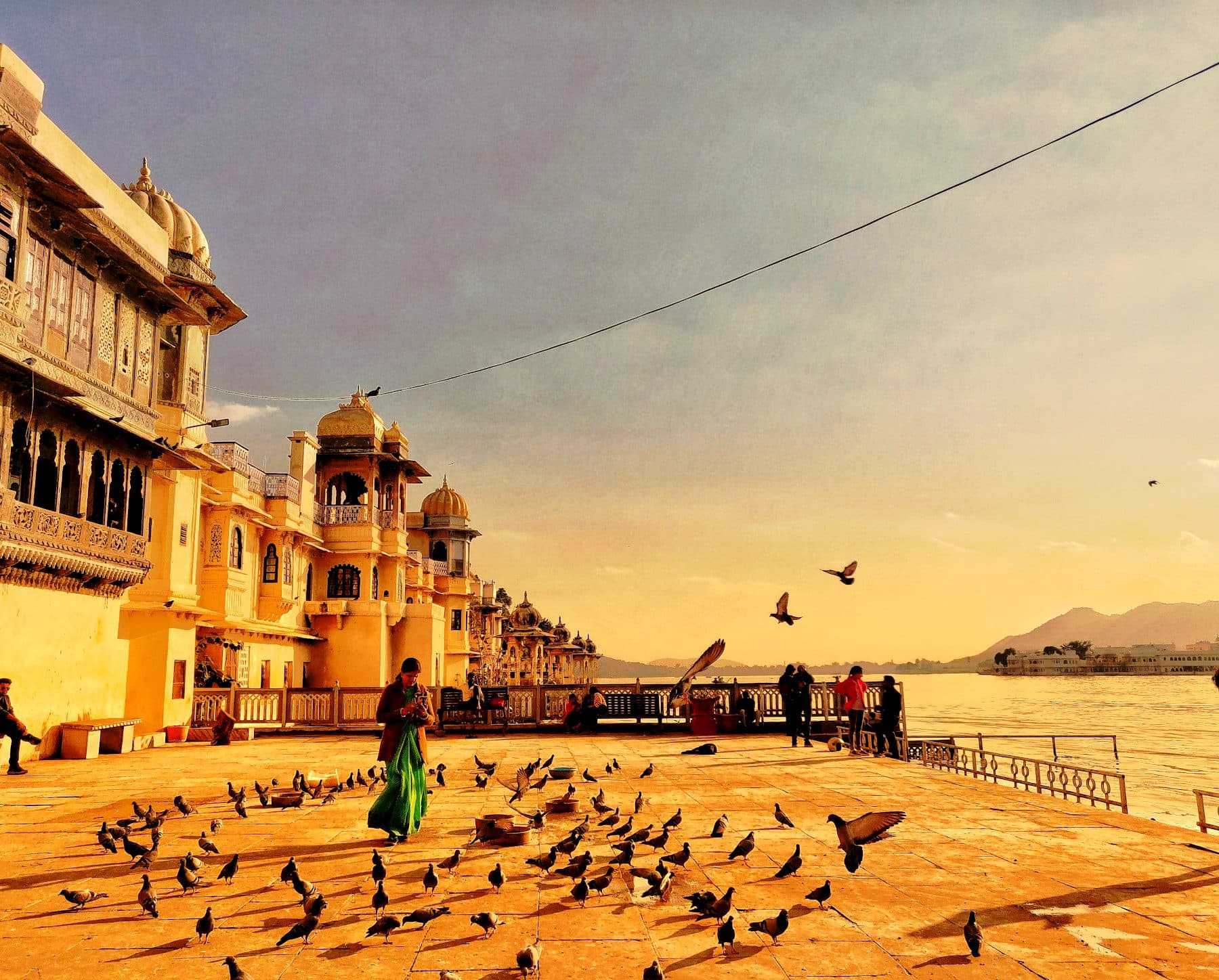 A Udaipur ghat below the old city, pigeons scattering across warm sandstone