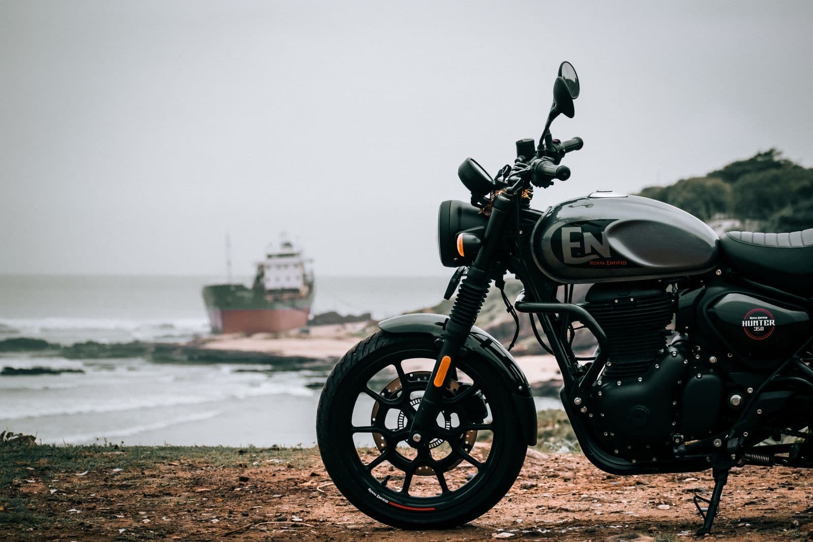 A black Royal Enfield Hunter 350 parked above a rocky beach